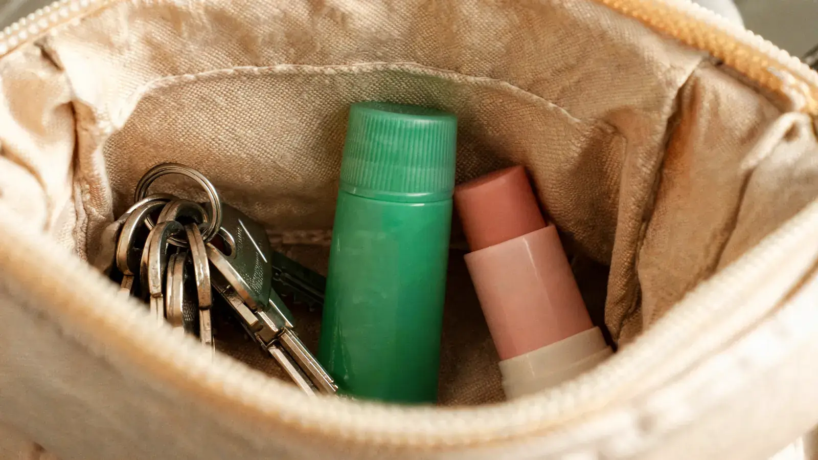 Small green tube of pain relief cream tucked into a purse alongside keys and lip balm