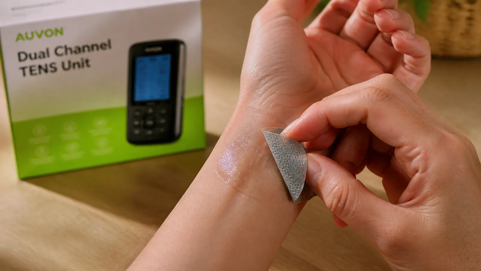 Close-up of a hand peeling a worn TENS electrode pad off skin, with sticky adhesive residue left on the skin surface