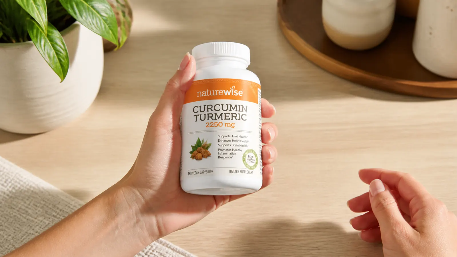 Hand picking up a bottle of NatureWise Curcumin Turmeric from a counter