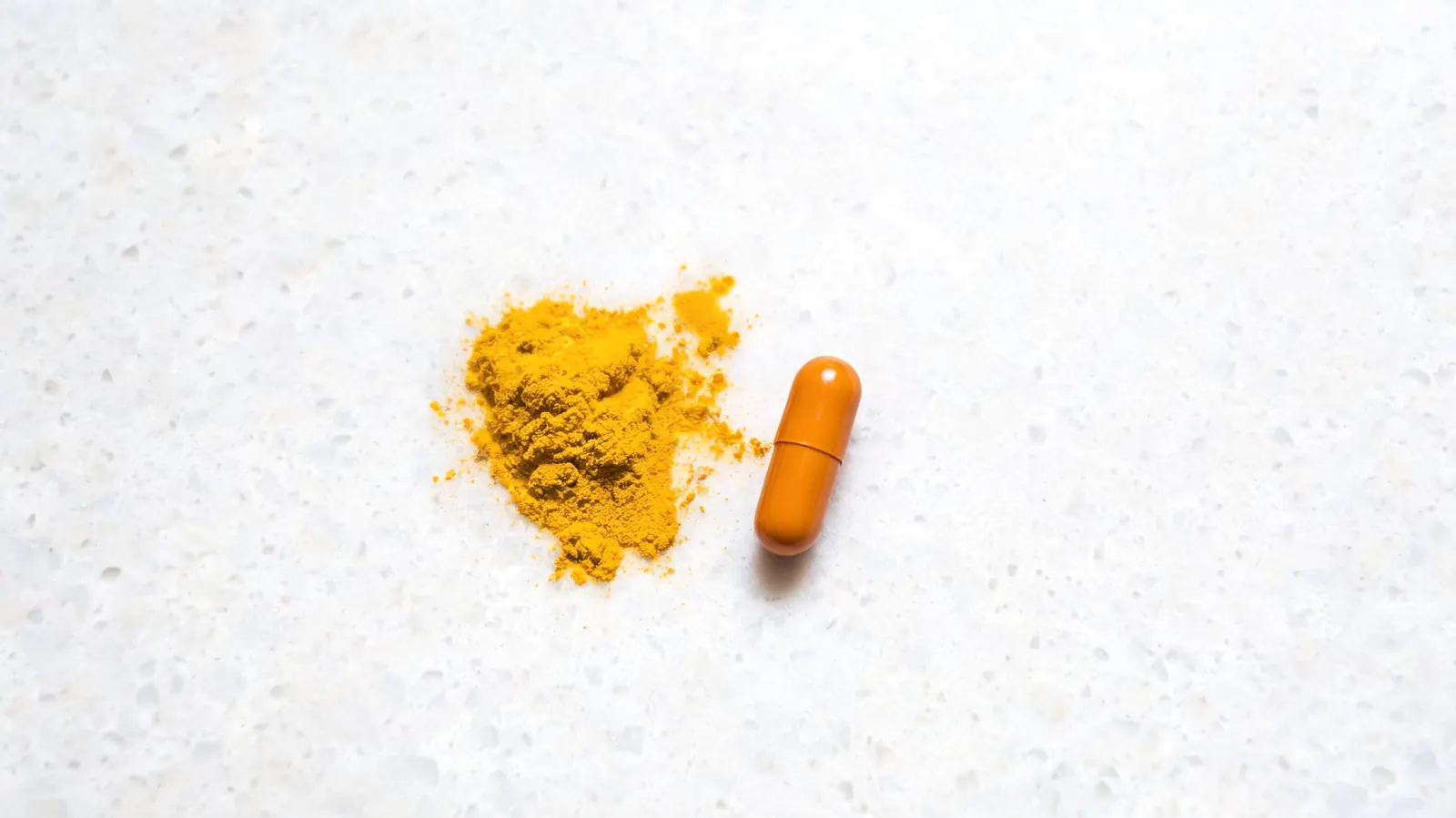 Yellow turmeric stain on a white bathroom countertop beside an open supplement bottle