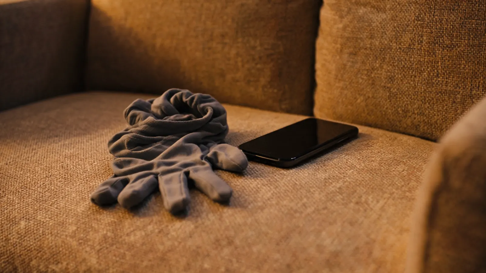 A single compression glove discarded on a sofa cushion beside a phone, the other glove absent, suggesting the gloves were taken off in the middle of the night